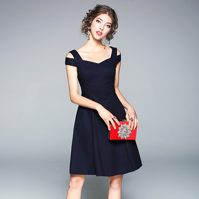 Donna in abito nero elegante con borsa rossa decorata, posa su sfondo grigio. Moda femminile, abbigliamento da sera, accessori di lusso.