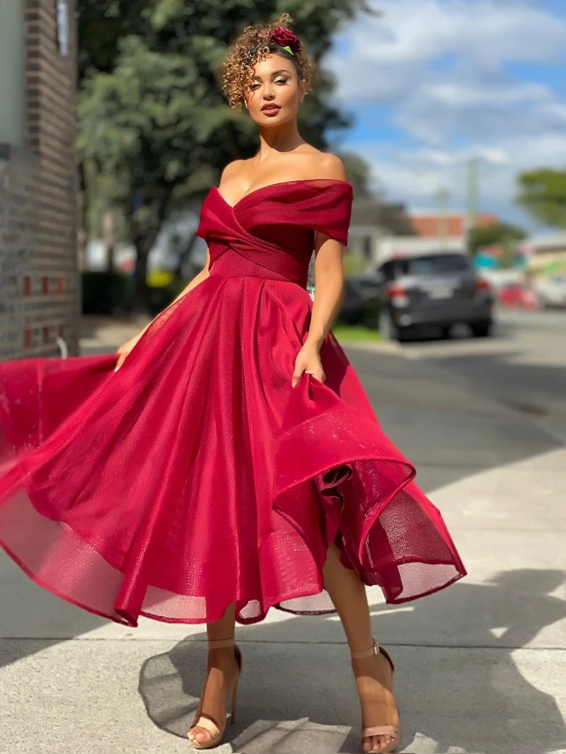 Donna con abito rosso elegante, scollo a cuore, posa all'aperto su marciapiede. Moda femminile, abbigliamento da sera, stile glamour.