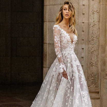 Abito da sposa elegante in pizzo floreale, maniche lunghe trasparenti, scollatura profonda, ambientato in un contesto architettonico classico.