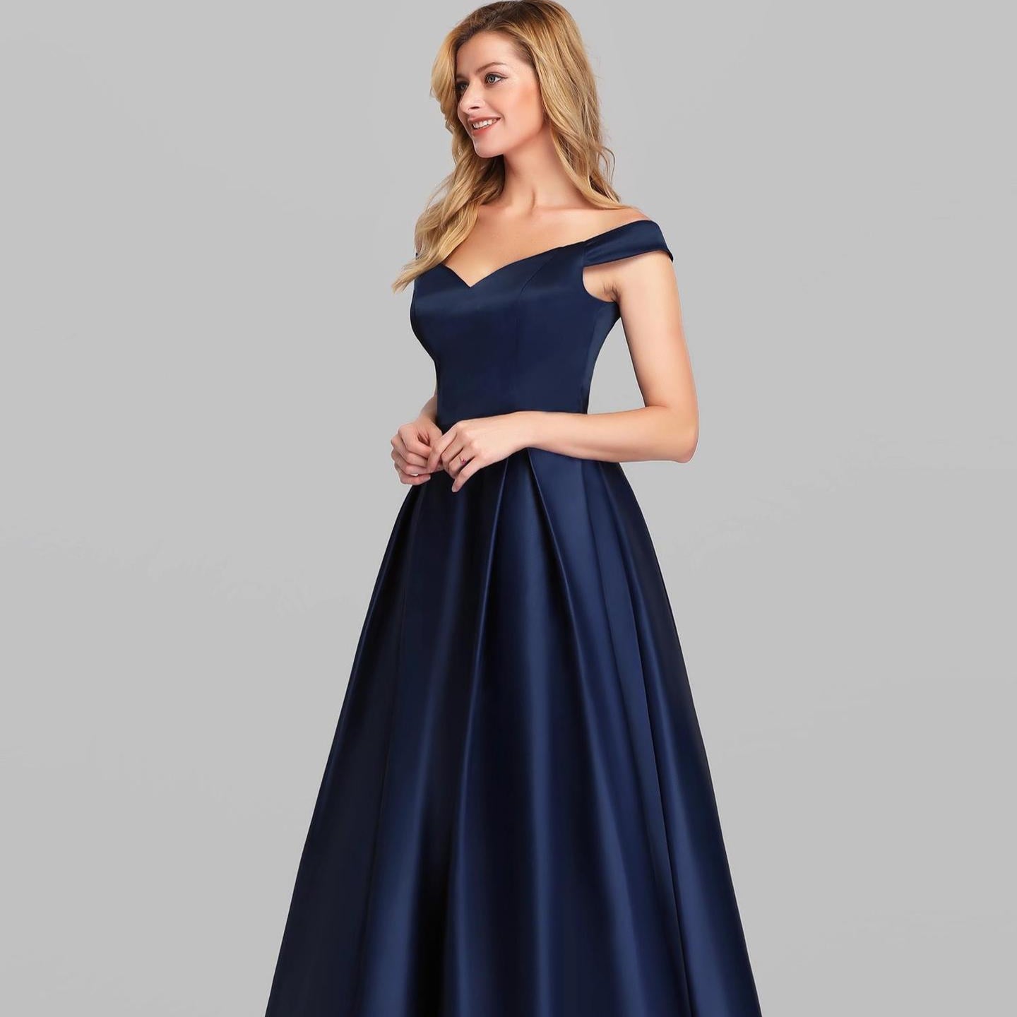 Donna in abito da sera blu scuro elegante, scollo a cuore, spalle scoperte, su sfondo grigio. Moda femminile, abbigliamento formale.
