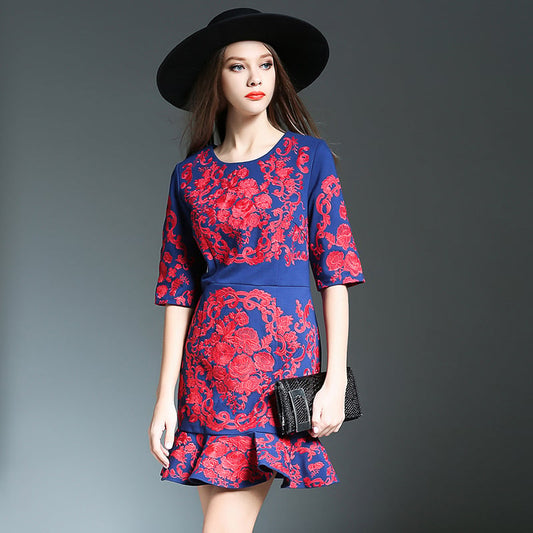 Donna con abito floreale blu e rosso, cappello nero, borsa a mano. Moda elegante, stile autunnale, abbigliamento femminile di tendenza.