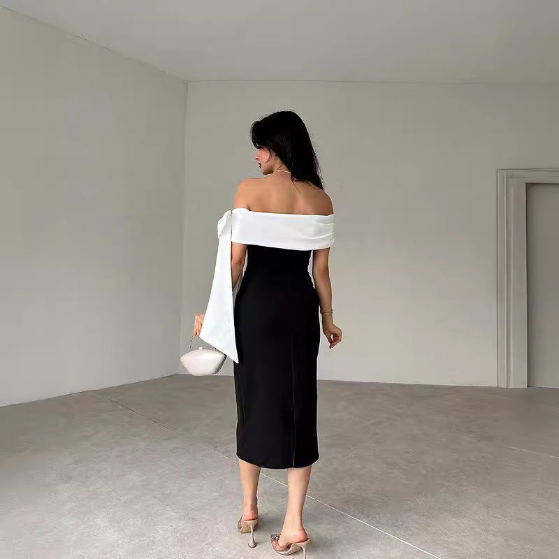 Donna in abito nero elegante con spalle scoperte, borsa bianca, tacchi alti, in una stanza minimalista. Moda femminile, stile sofisticato.