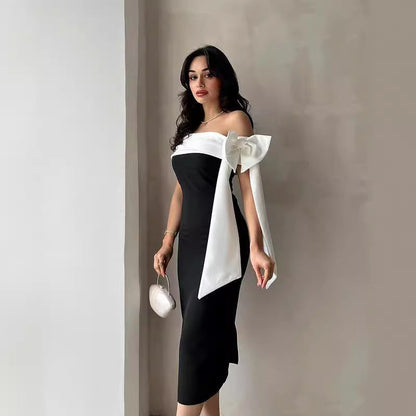Donna in abito elegante nero e bianco con fiocco, posa con borsa a mano. Moda femminile, abbigliamento da sera, stile sofisticato.