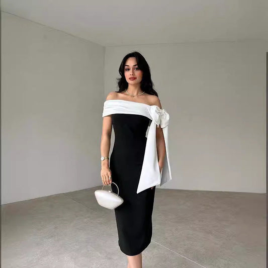 Donna in elegante abito nero con spalle scoperte e fiocco bianco, borsa a mano chiara. Moda femminile, stile sofisticato, abbigliamento da sera.