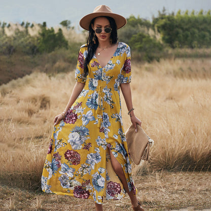 Donna con abito floreale giallo, cappello a tesa larga e occhiali da sole, in un campo estivo. Moda estiva, stile boho-chic, abbigliamento femminile.