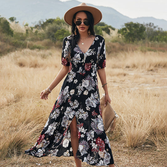 Donna con abito floreale nero, cappello a tesa larga, occhiali da sole, in un campo aperto. Moda estiva, stile boho-chic, abbigliamento casual.