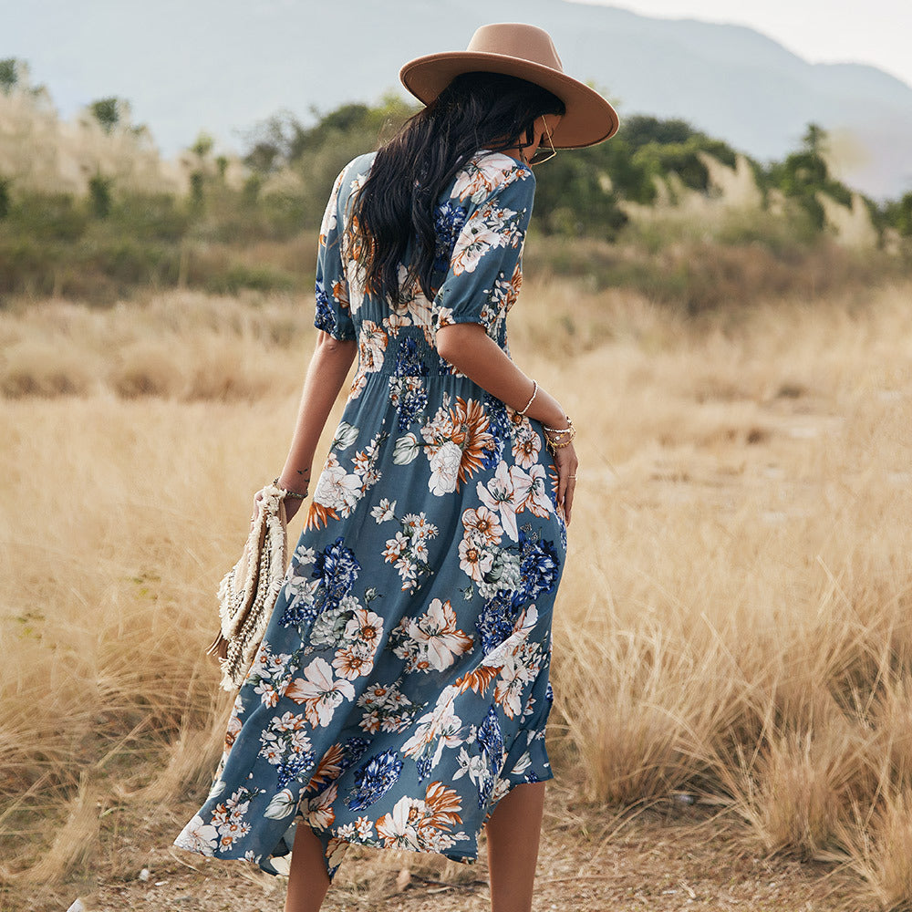 Donna con abito floreale blu, cappello beige, cammina in un campo. Moda estiva, stile boho, natura, abbigliamento femminile casual.