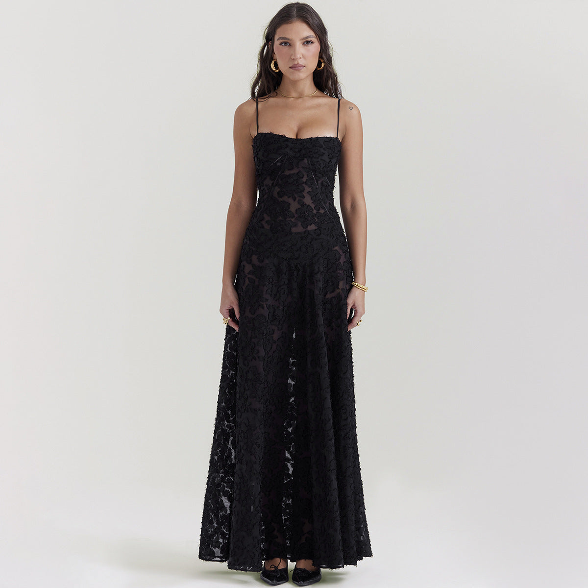 Donna in abito lungo nero elegante con spalline sottili, motivo floreale trasparente, posa su sfondo neutro. Moda femminile, abbigliamento da sera.