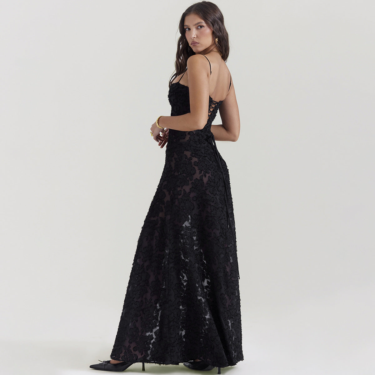 Donna in abito lungo nero elegante con pizzo, spalline sottili, posa laterale. Moda femminile, abbigliamento da sera, stile sofisticato.