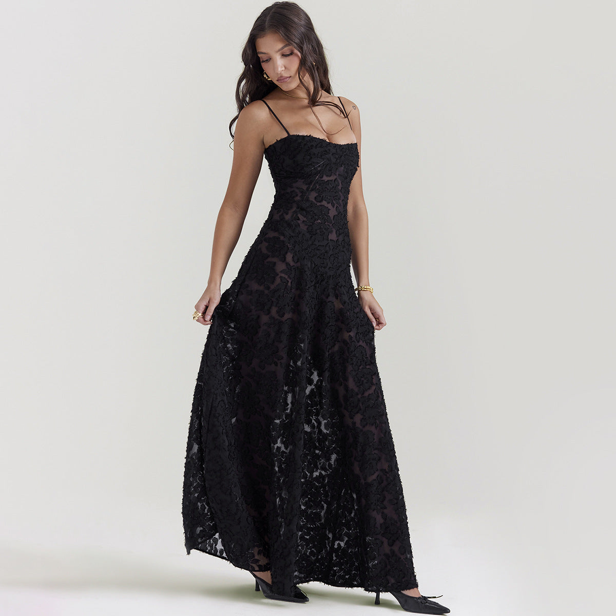 Donna in abito lungo nero elegante, con spalline sottili e motivo floreale, posa su sfondo neutro. Moda femminile, abbigliamento da sera.