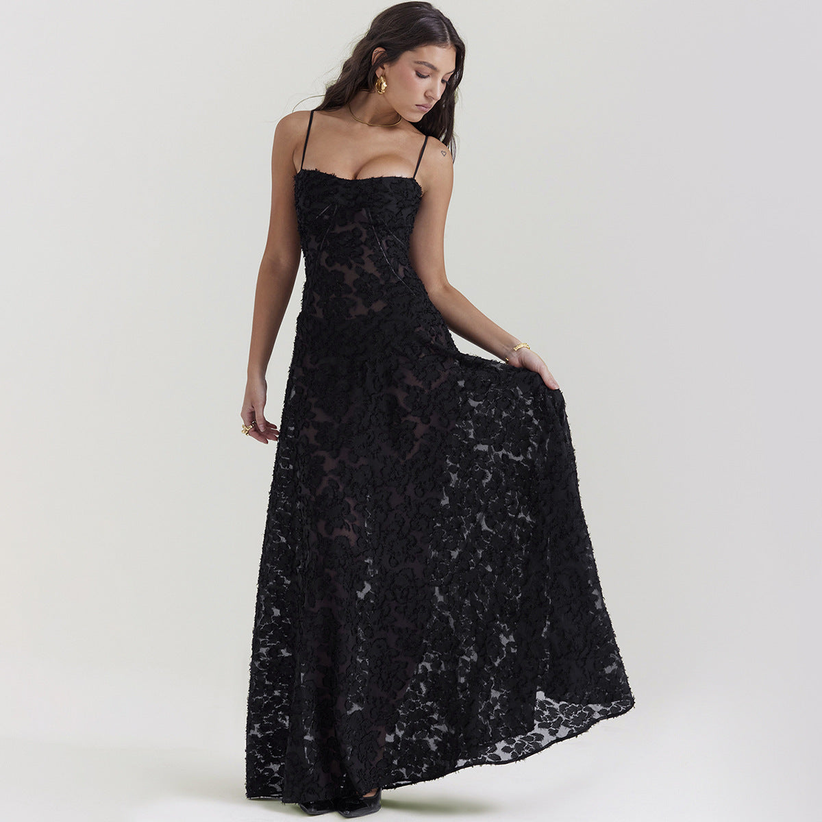 Donna in abito lungo nero elegante con pizzo, posa su sfondo neutro. Moda femminile, abbigliamento da sera, stile sofisticato.