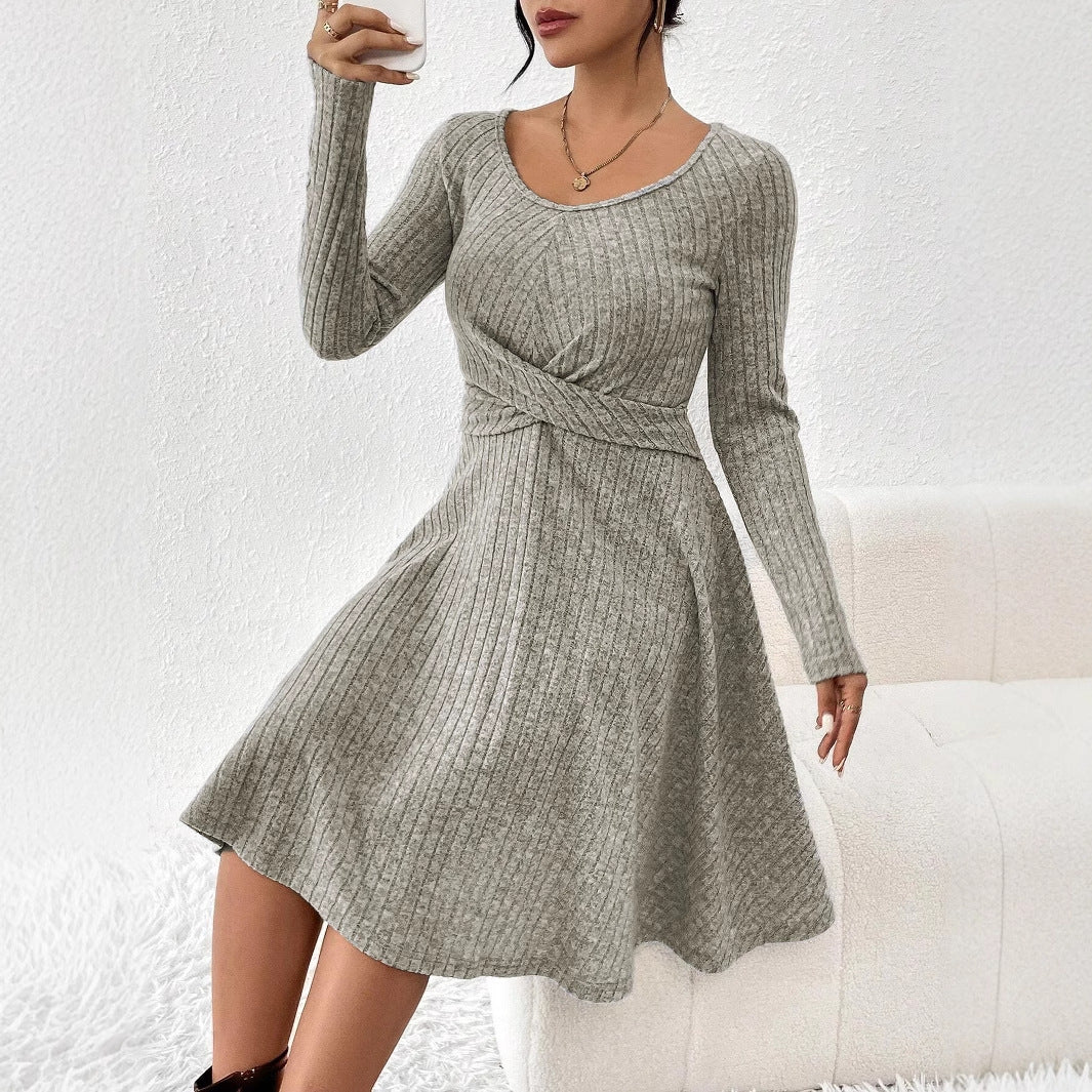 Donna con abito grigio a coste, maniche lunghe, scollo a V, seduta su divano bianco. Moda autunnale, stile casual elegante.