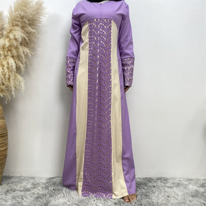 Abito lungo elegante viola e beige con dettagli in pizzo, sfondo bianco, tappeto grigio, pianta decorativa a sinistra. Moda femminile, abbigliamento formale.