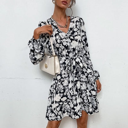 Donna con abito floreale bianco e nero, borsa a tracolla beige, collana argento. Moda elegante, stile casual chic, tendenze abbigliamento femminile.