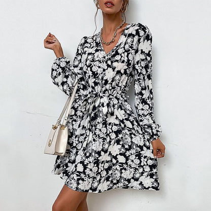 Abito floreale bianco e nero con maniche lunghe e cintura, indossato da una donna con borsa a tracolla chiara. Moda elegante e casual.