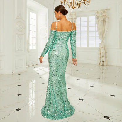 Donna in abito lungo verde smeraldo con paillettes, in una stanza elegante con pavimento in marmo e lampadario. Moda, eleganza, abito da sera.