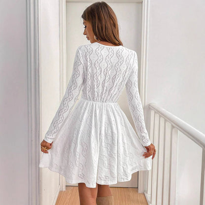 Donna in abito bianco elegante, maniche lunghe, motivo traforato, in piedi su una scala interna. Moda femminile, abbigliamento chic, stile moderno.