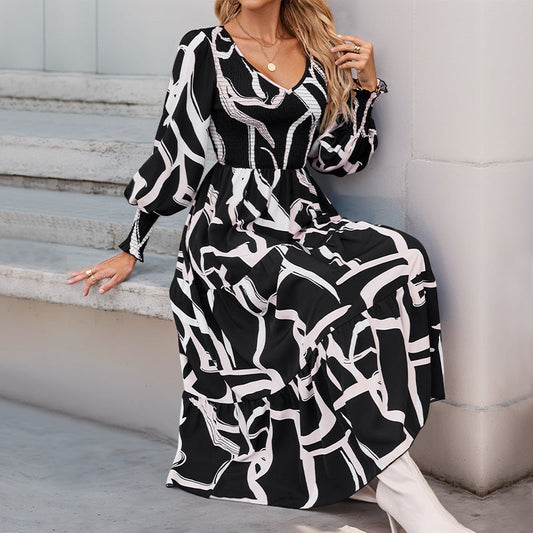 Donna seduta su gradini indossa un abito lungo a fantasia astratta bianco e nero, con maniche lunghe e scollo a V. Moda elegante, abbigliamento femminile.