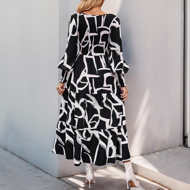 Donna con abito lungo nero e bianco a motivi geometrici, maniche lunghe, in piedi su marciapiede. Moda femminile elegante, stile moderno.