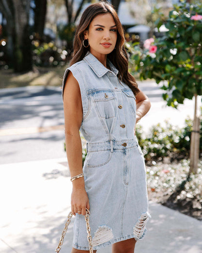 Donna con abito di jeans smanicato, bottoni frontali e strappi, in strada soleggiata. Moda casual, stile urbano, tendenza denim.