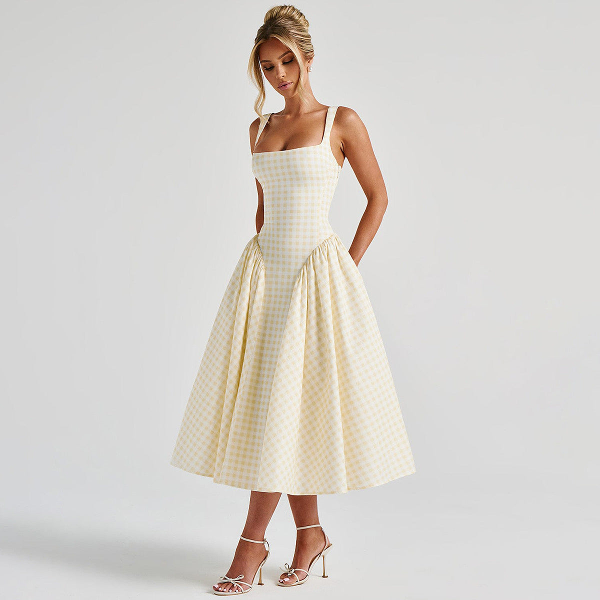 Donna in abito a quadri gialli e bianchi, stile vintage, con spalline sottili e gonna ampia. Moda elegante, abbigliamento estivo, tendenze 2023.