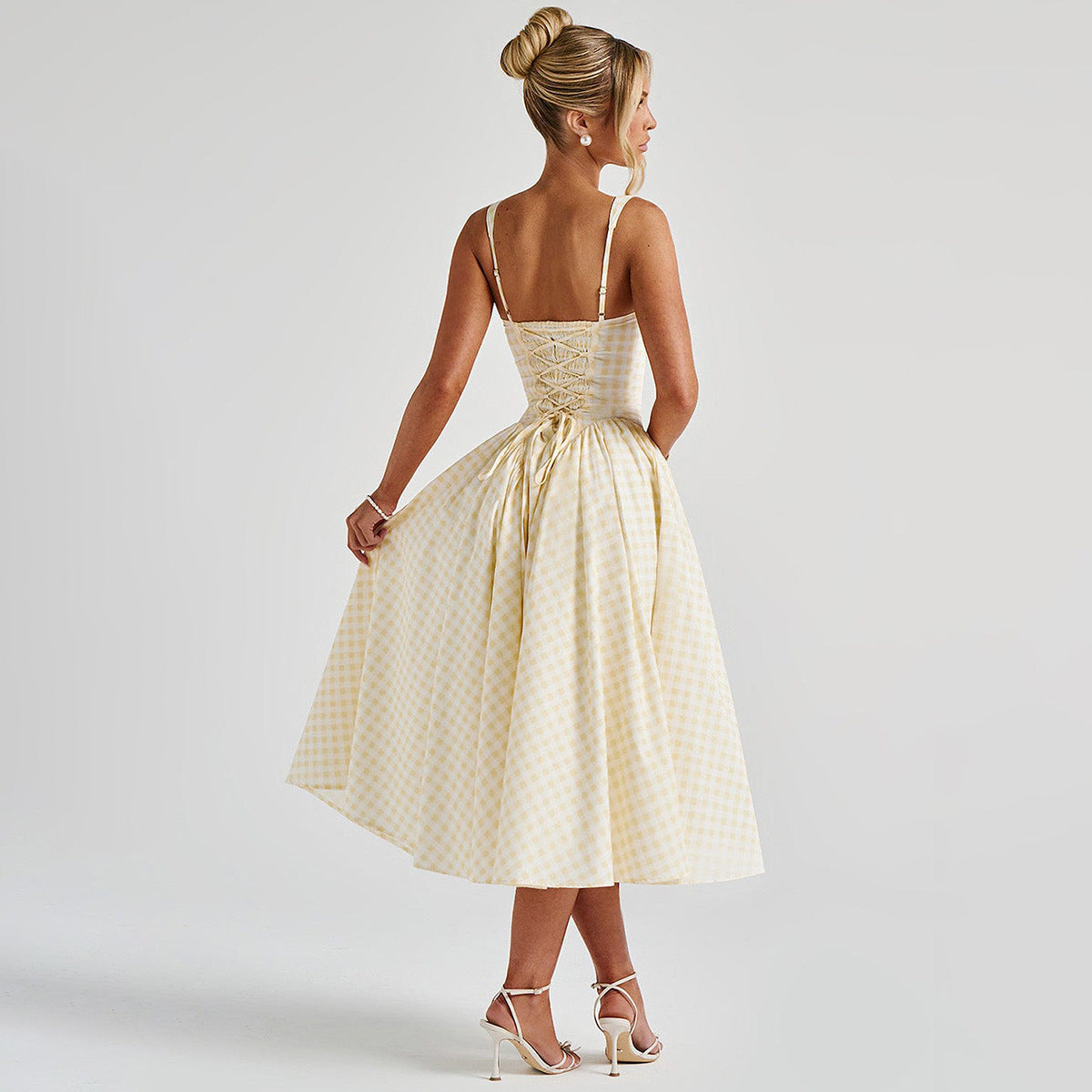 Donna in abito estivo a quadri gialli e bianchi, con corpetto a corsetto e gonna ampia, capelli raccolti, sandali bianchi eleganti.