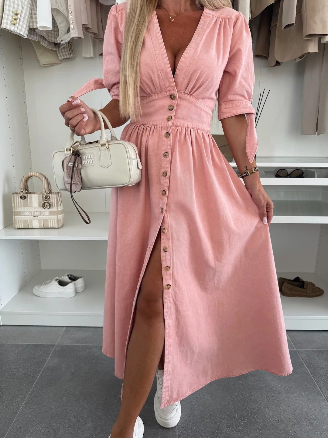 Donna in abito rosa con bottoni, borsa bianca a mano, scarpe bianche sullo sfondo. Moda femminile, abbigliamento estivo elegante.