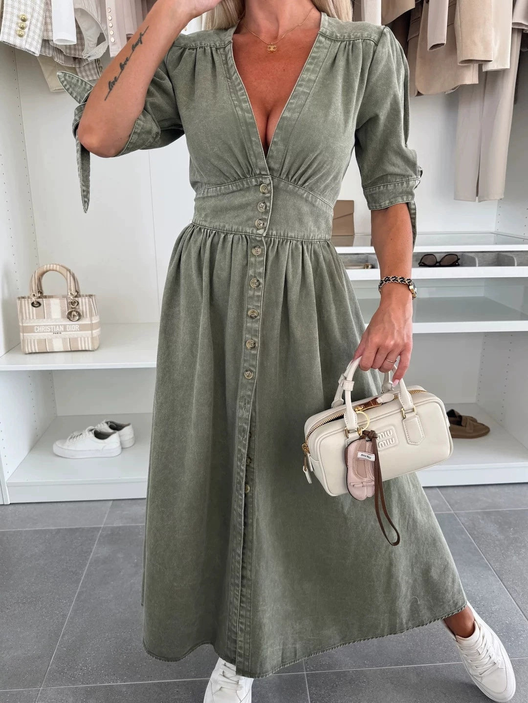 Donna in abito verde oliva con bottoni, borsa a mano bianca, scarpe da ginnastica bianche, in negozio di moda. Stile casual chic, moda femminile.