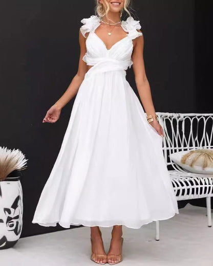 Abito lungo bianco estivo da donna con spalline arricciate, scollo a V, indossato con sandali beige. Sfondo nero e sedia bianca decorativa.