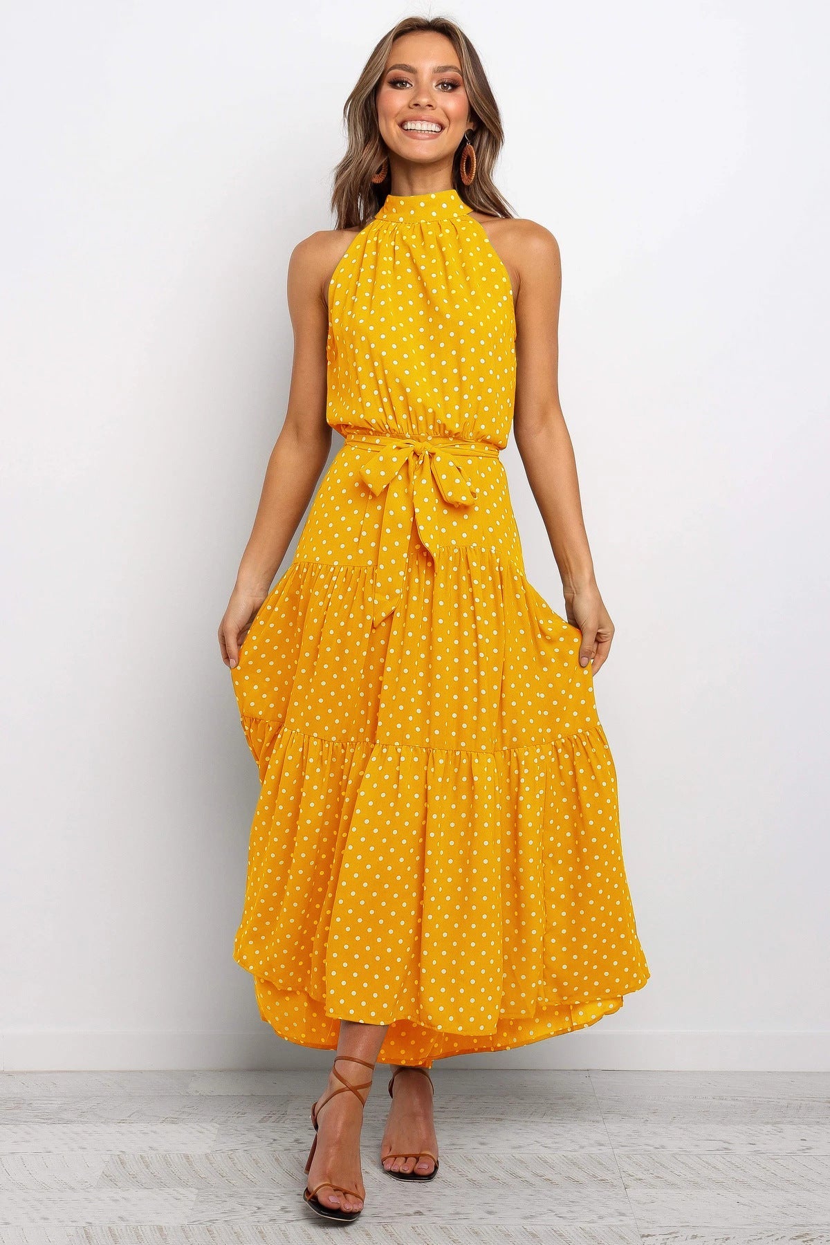 Donna sorridente in abito giallo a pois, lungo e senza maniche, con cintura in vita. Moda estiva elegante, abbigliamento femminile casual chic.