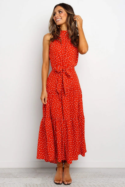 Donna sorridente in abito lungo rosso a pois bianchi, senza maniche, con cintura in vita. Moda estiva elegante, abbigliamento femminile casual.