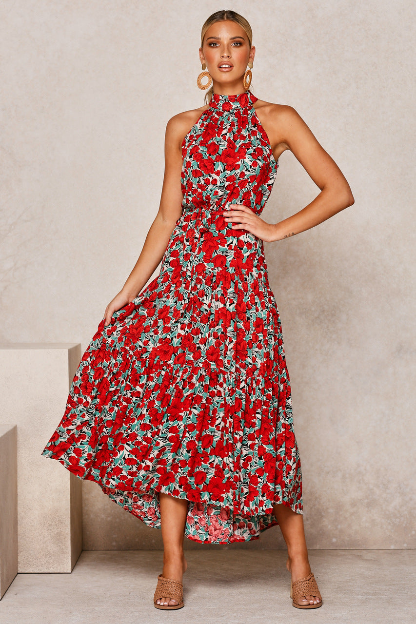 Donna in abito lungo floreale rosso con scollo all'americana, orecchini dorati e sandali beige. Moda estiva elegante e femminile.