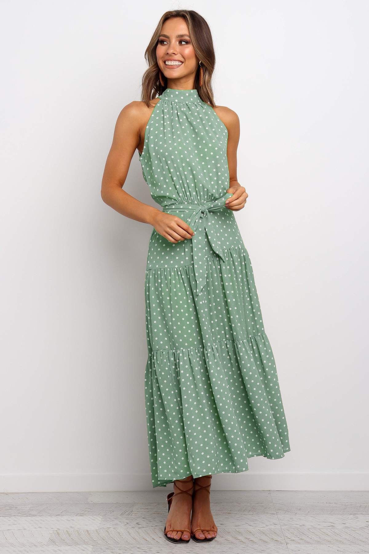 Donna sorridente in abito lungo verde a pois bianchi, senza maniche, con cintura in vita. Moda estiva elegante, abbigliamento femminile casual.