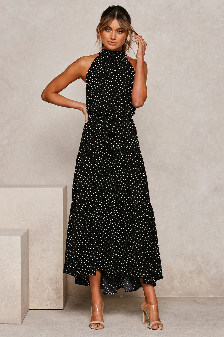 Donna in abito lungo nero a pois bianchi, elegante e moderno, posa su sfondo neutro. Moda femminile, abbigliamento estivo, stile chic.