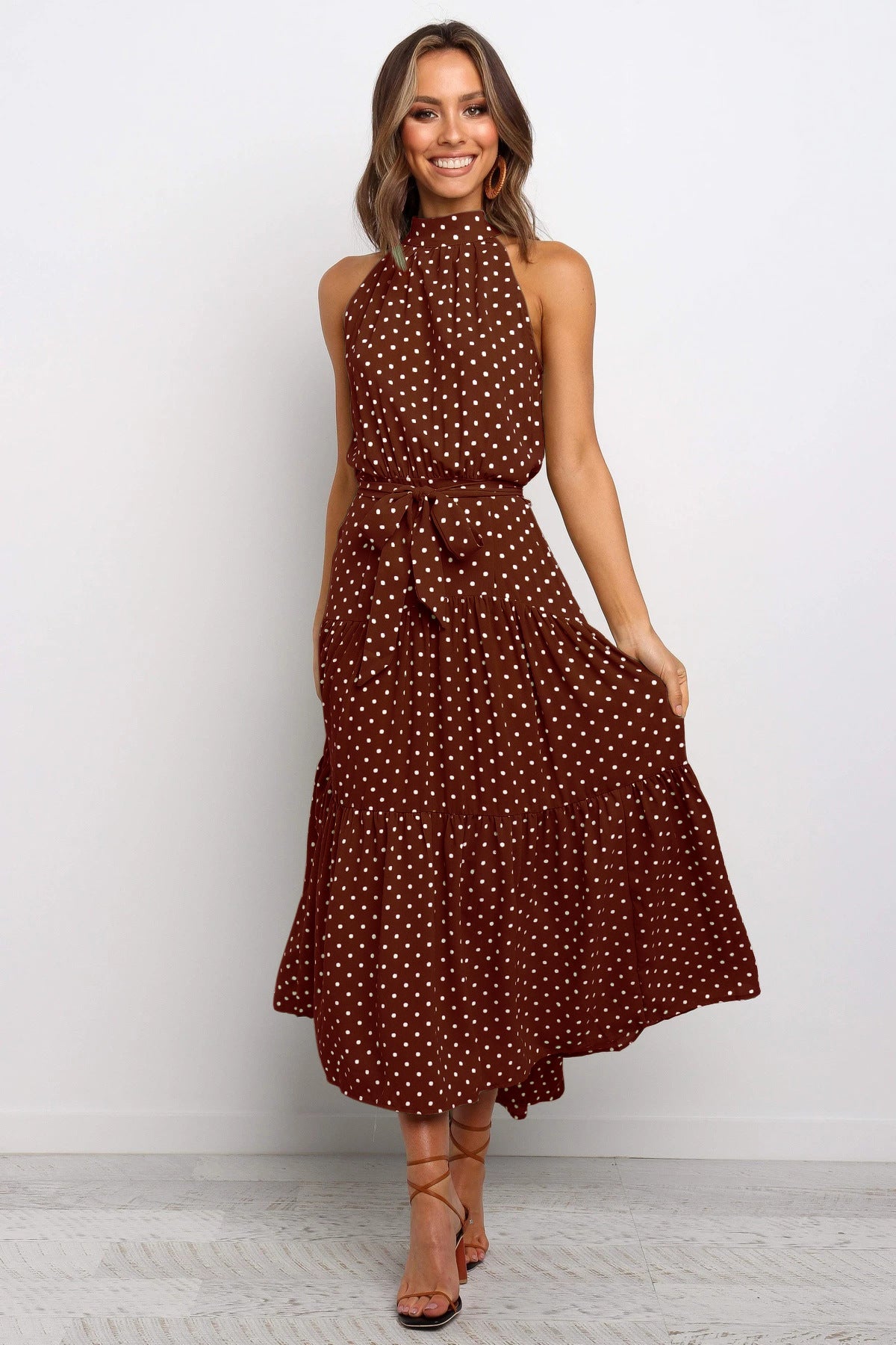 Donna con abito lungo marrone a pois bianchi, senza maniche, con cintura in vita. Moda elegante, abbigliamento estivo, stile casual chic.