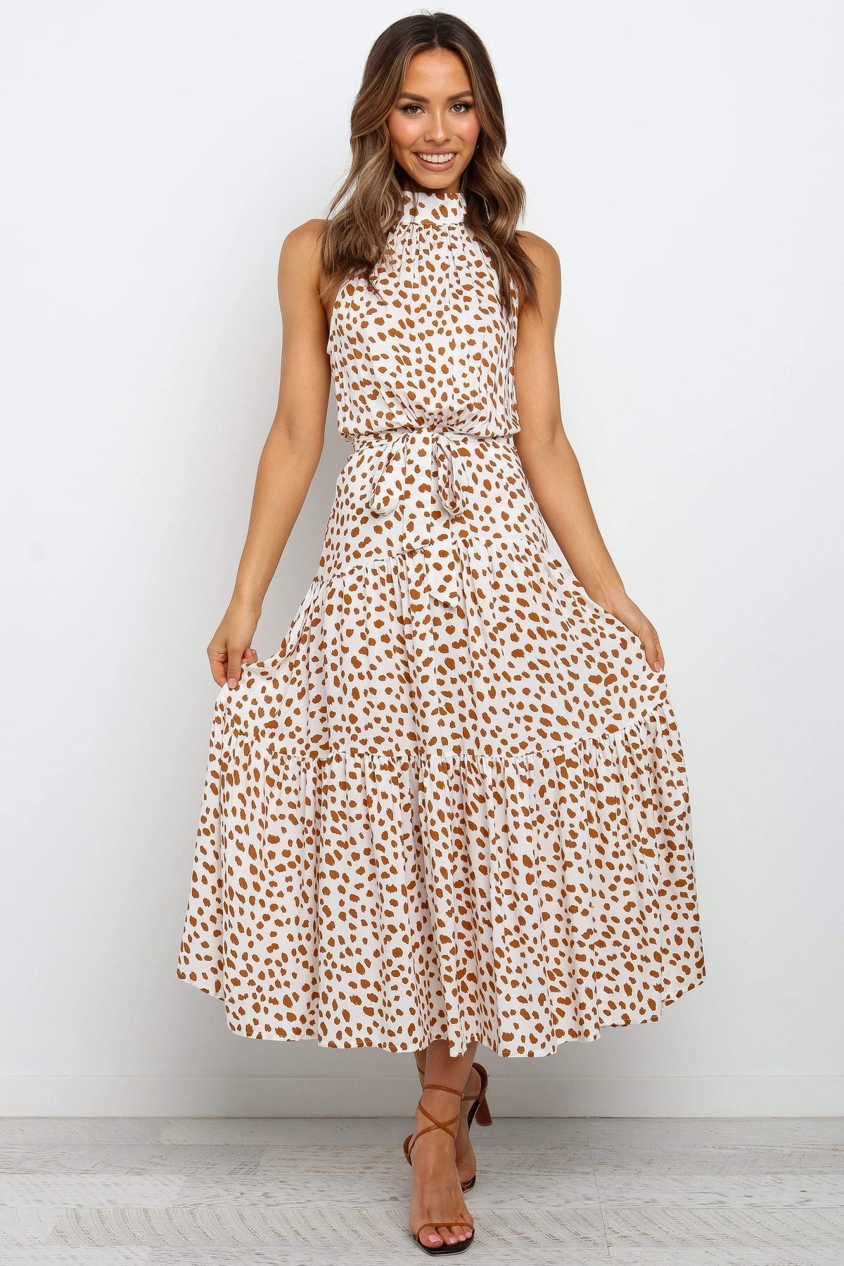 Donna in abito lungo a pois marroni su sfondo bianco, senza maniche, con cintura in vita. Moda estiva elegante, abbigliamento femminile casual.