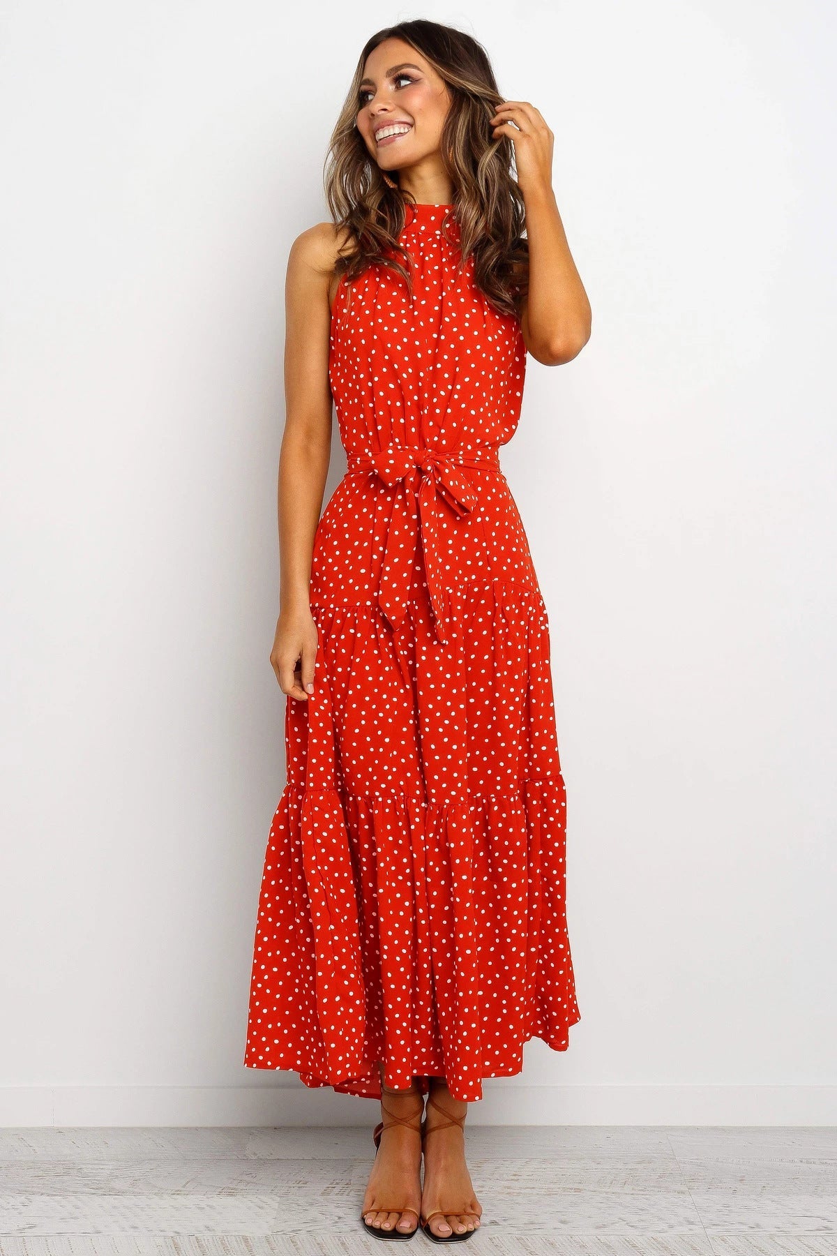 Donna sorridente in abito lungo rosso a pois bianchi, senza maniche, con cintura in vita. Moda estiva elegante, abbigliamento femminile casual.