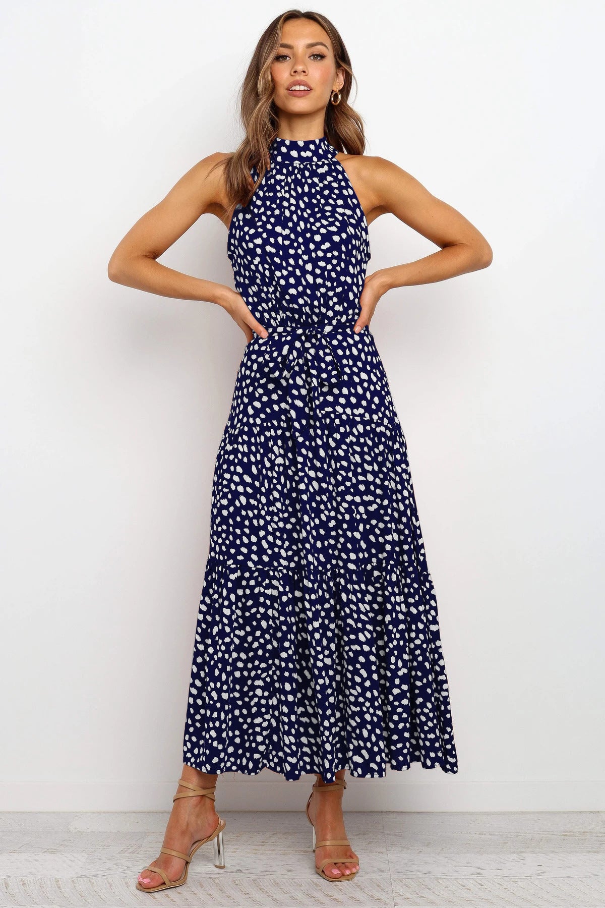 Donna in abito lungo blu a pois bianchi, senza maniche, con sandali dorati. Moda elegante, abbigliamento estivo, stile casual chic.