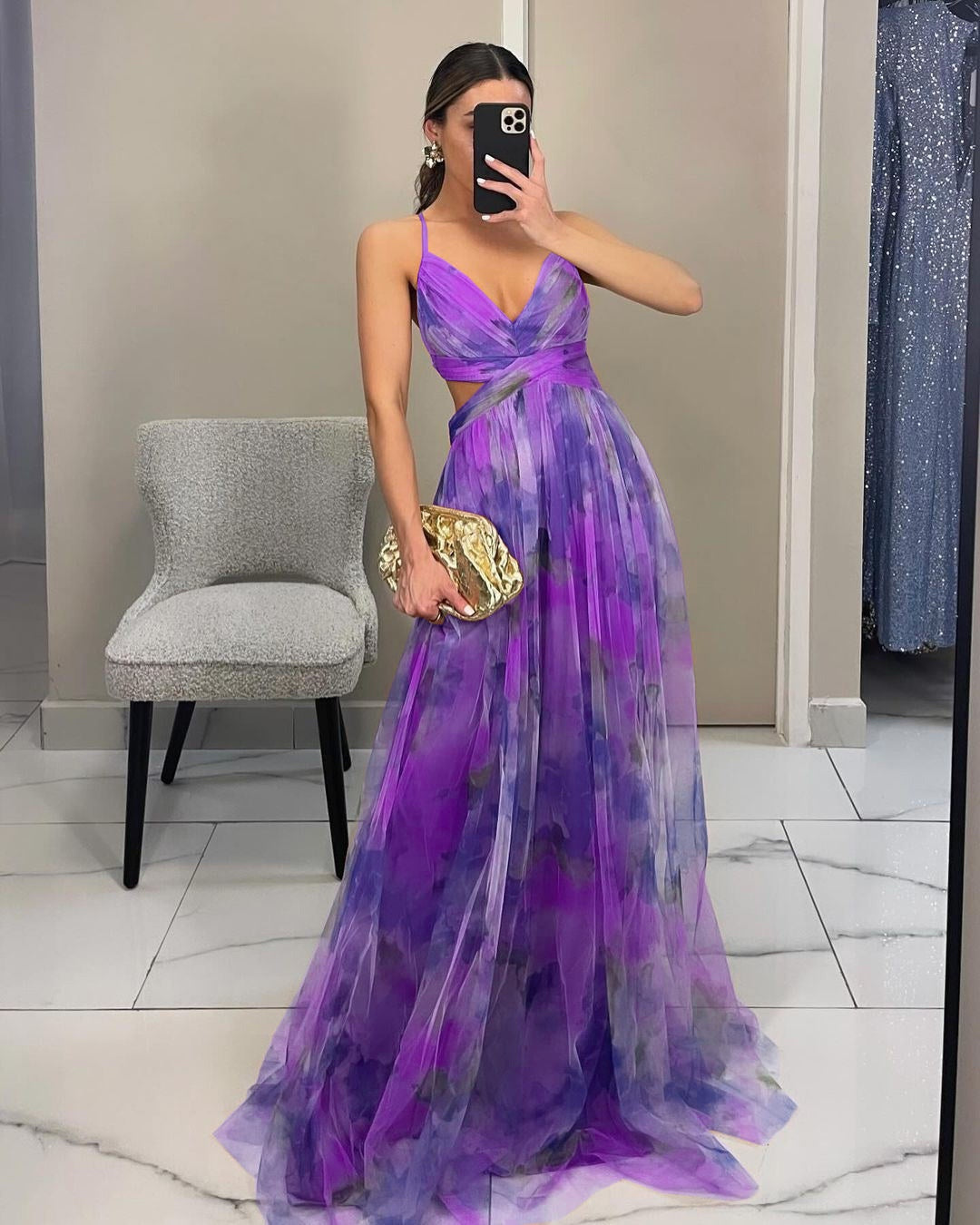 Donna in abito da sera viola con sfumature floreali, scatta un selfie. Vestito elegante, clutch dorata, moda femminile, tendenze abbigliamento 2023.