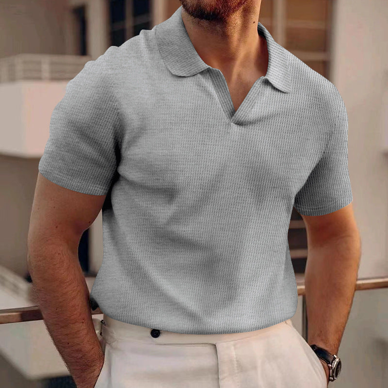 Uomo in maglietta grigia a maniche corte e pantaloni bianchi, appoggiato a una ringhiera. Moda maschile estiva, look casual ed elegante.