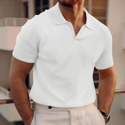 Uomo in camicia polo bianca, elegante e casual, su sfondo urbano. Moda maschile estiva, abbigliamento casual chic, stile contemporaneo.