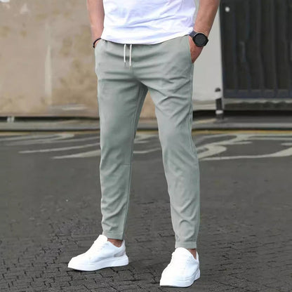 Uomo in pantaloni sportivi grigi e scarpe da ginnastica bianche su strada asfaltata. Look casual, moda maschile, abbigliamento urbano.