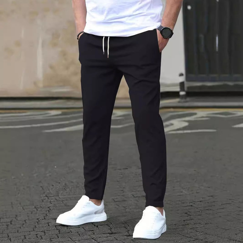 Uomo con pantaloni neri casual e scarpe da ginnastica bianche, in piedi su strada asfaltata. Stile urbano, moda maschile, abbigliamento casual.