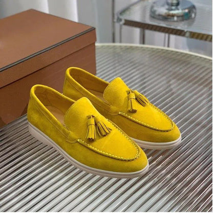 Scarpe mocassini gialle in pelle scamosciata con nappine, suola bianca, su tavolo metallico, scatola marrone sullo sfondo. Moda calzature eleganti.