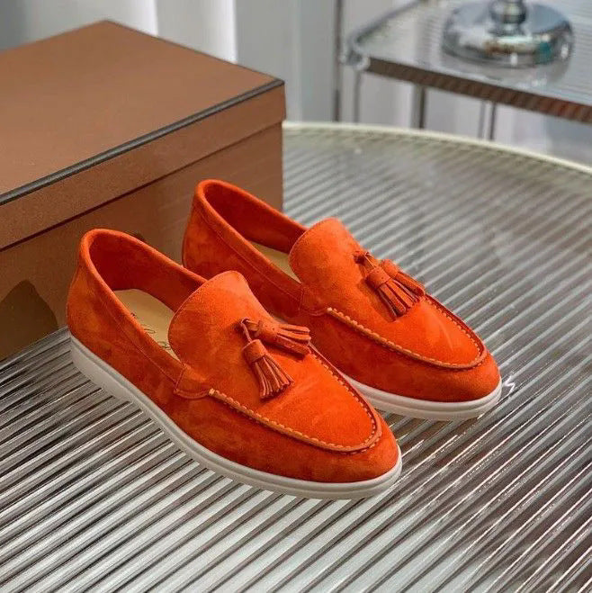 Scarpe mocassini arancioni in pelle scamosciata con nappine, suola bianca, su tavolo di vetro. Eleganti e moderne, perfette per moda uomo.