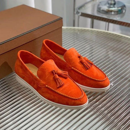 Scarpe mocassini arancioni in pelle scamosciata con nappine, suola bianca, su tavolo di vetro. Eleganti e moderne, perfette per moda uomo.