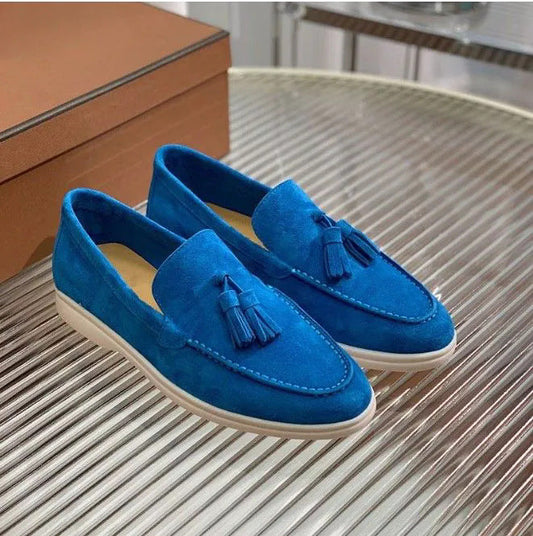Mocassini uomo in pelle scamosciata blu con nappine, suola bianca, su tavolo di vetro. Scarpe eleganti, moda maschile, calzature di lusso.