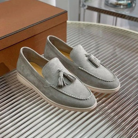Mocassini uomo in pelle scamosciata grigia con nappine, suola bianca, su tavolo di vetro. Scarpe eleganti, moda maschile, calzature di lusso.