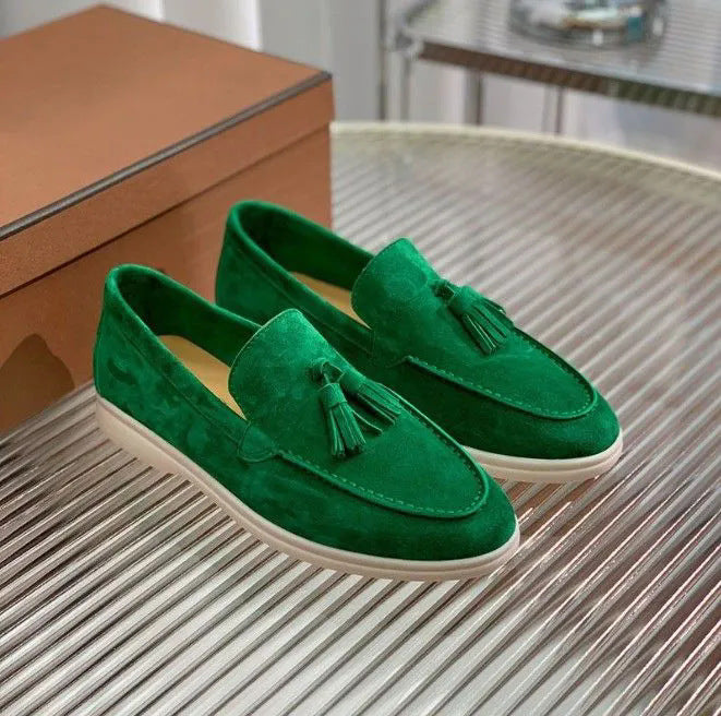 Scarpe mocassini verdi in velluto con nappine, suola bianca, su tavolo di vetro. Eleganti calzature uomo, moda casual, stile sofisticato.
