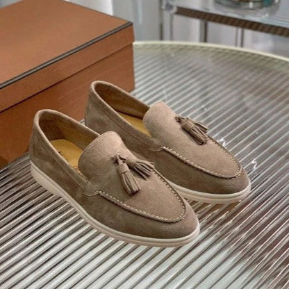 Mocassini beige in pelle scamosciata con nappine, suola bianca, su tavolo di vetro. Scarpe eleganti uomo, moda casual, calzature di lusso.